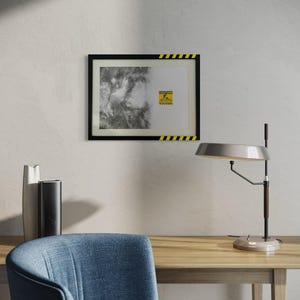 May include: A rectangular wall art piece in a black frame with yellow and black hazard stripes on the top and bottom edges. The print features a black and white abstract textured pattern on the left and a yellow caution sign on the right.