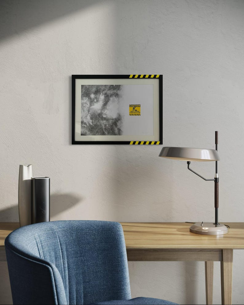 May include: A rectangular wall art piece in a black frame with yellow and black hazard stripes on the top and bottom edges. The print features a black and white abstract textured pattern on the left and a yellow caution sign on the right.