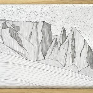 May include: A framed black and white line art drawing of a mountain range. The artwork features intricate vertical lines defining the rocky peaks and slopes, set against a sky filled with small black dots. The piece is enclosed in a light wood frame.