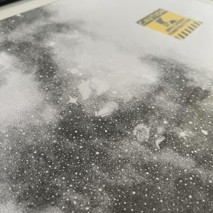 May include: A black and white stippled art print featuring a dense field of stars and nebulae. A small yellow rectangular sticker is positioned in the upper right corner, displaying the text CAUTION AREA UNDER CONSTRUCTION with a graphic icon.