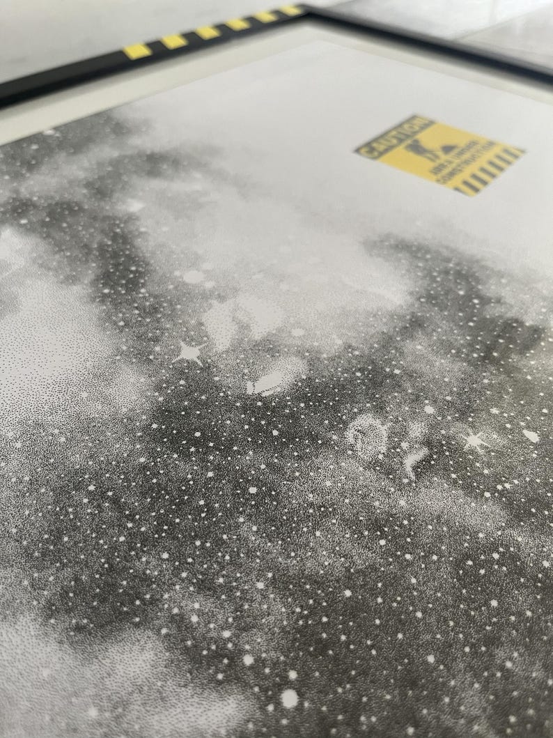 May include: A black and white stippled art print featuring a dense field of stars and nebulae. A small yellow rectangular sticker is positioned in the upper right corner, displaying the text CAUTION AREA UNDER CONSTRUCTION with a graphic icon.