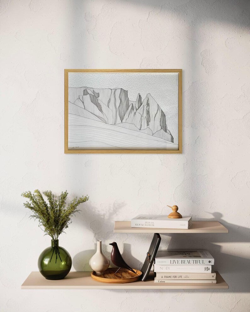 May include: A framed horizontal line art print featuring a mountain landscape with jagged peaks and textured stippling, displayed in a light wood frame. The artwork depicts a rocky mountain range with fine black lines on a white background.