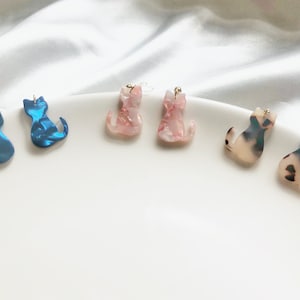 以下が含まれることがあります： 猫の形をしたイヤリングが5ペア。2ペアは青、2ペアは白の模様が入ったピンク、1ペアは白の模様が入った茶色です。