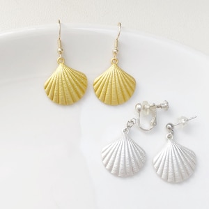Könnte beinhalten: Ohrringe in Muschelform in Gold und Silber. Die goldenen Ohrringe haben einen Hakenverschluss, während die silbernen Ohrringe Clip-On- und Stecker-Optionen umfassen. Die Ohrringe werden auf einer weißen Oberfläche präsentiert.