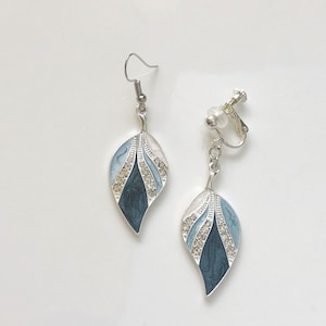 Può includere: Un paio di orecchini a forma di foglia. Un orecchino ha un gancio, l'altro è a clip. Ogni orecchino presenta un design in metallo argentato con finitura smaltata blu, bianca e blu scuro. Il design è impreziosito da piccoli strass trasparenti.