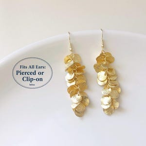 May include: Gold-coloured dangle earrings with a layered, cascading design. The earrings are made of small, round, textured metal pieces. The text "Fits All Ears: Pierced or Clip-on" is visible in a circular graphic.