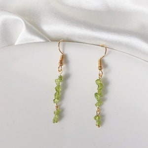 Puede incluir: Un par de pendientes de oro con una cadena colgante de cuentas de piedras preciosas de color verde claro.