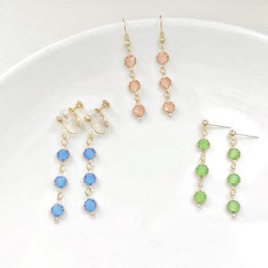 May include: Three pairs of dangle earrings with gold-tone chains and colourful crystal beads. The earrings on the left have blue beads, the earrings in the middle have peach beads, and the earrings on the right have green beads.