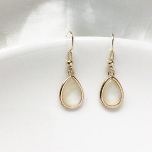 Puede incluir: Un par de pendientes de gota de oro con piedras nacaradas blancas.