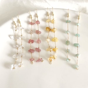 May include: Five pairs of long, gold chain earrings with different colored gemstone chips. The earrings are arranged in a row on a white surface.
