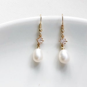 May include: A pair of gold earrings with a small clear crystal and a white pearl drop.