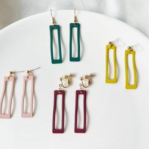 May include: A selection of rectangular earrings in shades of green, pink, yellow, and burgundy. Some have hooks, others are clip-ons. The earrings are presented on a white surface, showcasing their different designs.