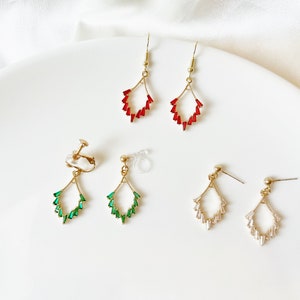 May include: A collection of gold-toned earrings with various designs. The earrings feature red, green, and clear crystal accents. Styles include hook, clip-on, and stud earrings, all arranged on a white surface.