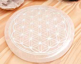 May include: A white selenite charging plate with a carved flower of life design. The plate is round and has a smooth, polished surface.