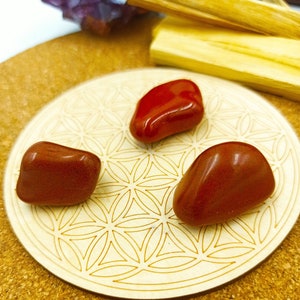 Peut inclure: Trois pierres de jaspe rouge lisses et polies sur un dessous de verre en bois avec un motif de fleur de vie.