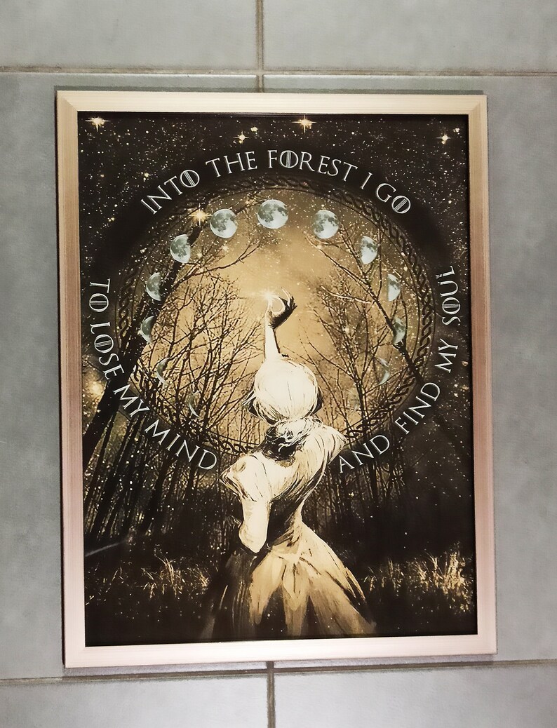 May include: A framed art print with a rose gold border. The artwork depicts a woman in a dress reaching towards a light source within a forest scene. The text reads "Into the forest I go to lose my mind and find my soul."