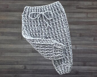May include: A pair of light gray crochet pants featuring a textured ribbed stitch pattern, a high waistband with a decorative drawstring bow, and fitted cuffs at the bottom of each leg, crafted from a soft yarn material.