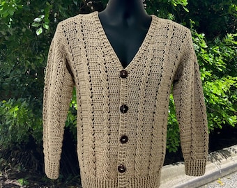 May include: A tan crochet cardigan featuring a V-neckline, long sleeves, and a front button closure with five dark brown circular buttons. The garment displays a vertical textured stitch pattern throughout the body and sleeves, with ribbed cuffs.