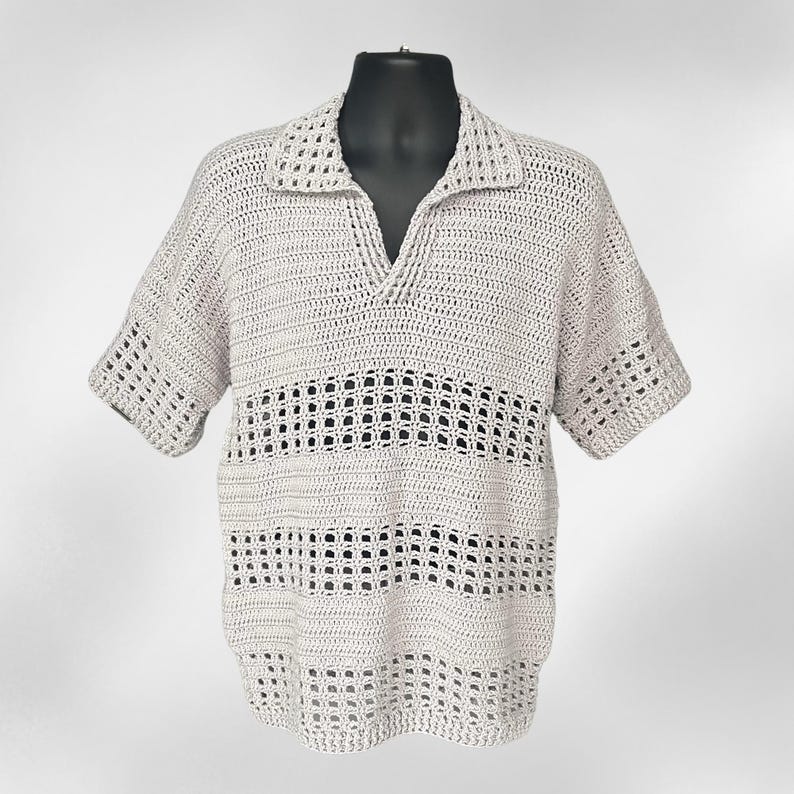 May include: A light beige, short-sleeved crochet shirt with a V-neck collar. The shirt features a textured, open-weave design with horizontal bands of larger open spaces. The shirt is displayed on a black mannequin.