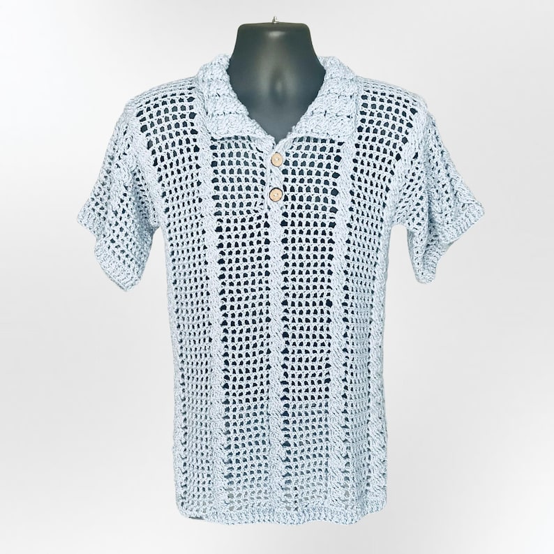 May include: A light blue crochet polo shirt with short sleeves and a collared neckline. The shirt features a button-down front with two wooden buttons. The open weave design is visible throughout the shirt, creating a textured appearance.