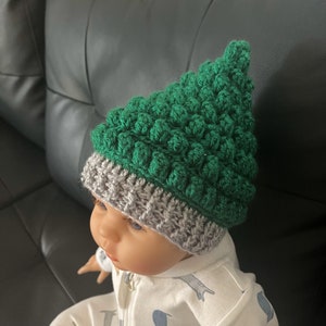 May include: A green and gray crocheted hat with a textured design. The hat is made with a bobble stitch and has a pointed top.