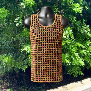 May include: A sleeveless crochet tank top featuring an open grid pattern. The garment is crafted from yarn in a variegated color palette of orange, yellow, and dark green, creating a textured, net-like appearance with a round neckline.