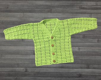 May include: A lime green long-sleeve cardigan featuring an open-work crochet pattern and a V-neckline. The garment is fastened down the center front with four small, round, light brown wooden buttons arranged in a vertical line.