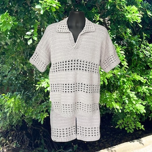 May include: A light beige crochet short-sleeve shirt featuring a collared neckline with a V-shaped opening. The garment is constructed with alternating bands of solid crochet stitches and openwork grid patterns throughout the body and sleeves.