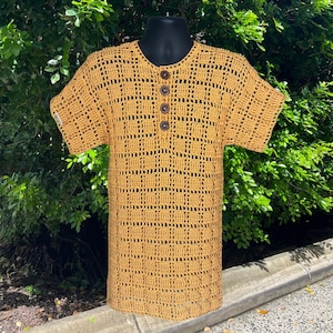 May include: Mustard yellow crochet top with a v-neck and short sleeves. The top features a button-up front with four brown buttons. The open weave design creates a grid-like pattern. The shirt is displayed on a black mannequin.
