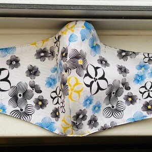 May include: A white face mask with a black and white floral pattern and blue and yellow accents.