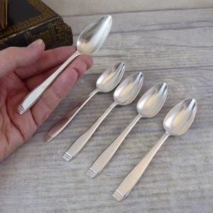 May include: Five silver spoons with a rounded, pointed end. The spoons are arranged in a row from largest to smallest.