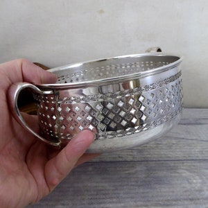 Könnte beinhalten: Silberne Schale mit zwei Griffen und einem dekorativen Muster aus Diamanten und Blättern. Die Schale ist aus Silber und hat eine glänzende Oberfläche.