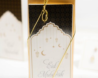 May include: A set of greeting cards with a gold and black geometric pattern. The cards feature a white arch with hanging lanterns and crescent moons. The text "Eid Mubarak" is written in a decorative script.