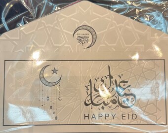 May include: A white card with a crescent moon and star design. The card has a geometric pattern and the text "Happy Eid" in English and Arabic.