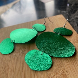 Peut inclure: Une paire de boucles d'oreilles en métal vert avec une finition texturée. Les boucles d'oreilles sont composées de plusieurs cercles qui se chevauchent.