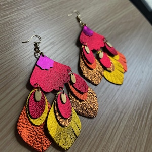 May include: A pair of dangle earrings with multiple layers of leather in shades of red, orange, and yellow. The earrings have a gold-tone finish and are accented with small, round, gold-tone beads.