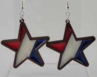 May include: A pair of star-shaped earrings with red, white, and blue paint. The earrings are made of wood and have silver hooks.