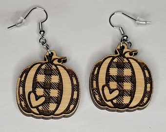 May include: A pair of wooden earrings shaped like pumpkins with a checkered pattern and a small heart on each. The earrings are brown and have silver hooks.
