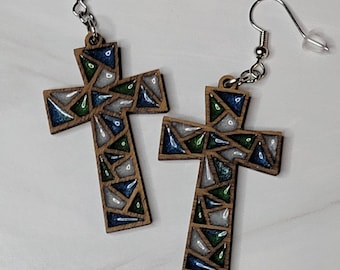 May include: A pair of wooden cross earrings with a stained glass design. The crosses are made of wood and have a blue, green, and white stained glass design. The earrings are silver and have a hook closure.