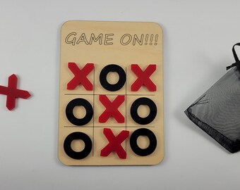May include: A wooden tic-tac-toe game with red X's and black O's. The game board says "GAME ON!!!" and comes with a black drawstring bag.