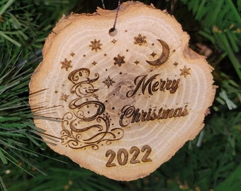 May include: A wooden Christmas ornament with a rustic brown finish. It features a stylized snowman design, the words "Merry Christmas", and the year "2022" burned into the wood.