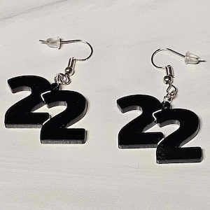 May include: A pair of black acrylic earrings shaped like the number 22. The earrings are attached to silver hooks.