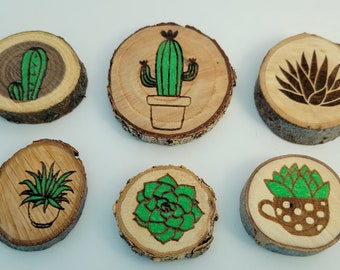 May include: Six wooden slices with different green succulent plants burned into the wood. The plants are in pots and include a cactus, aloe vera, and a succulent in a polka dot pot.