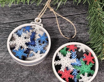 May include: Two round Christmas ornaments with snowflake designs. One ornament features white, blue, and dark blue snowflakes, while the other has red, green, and white snowflakes. Both ornaments have a white frame and are suspended by twine.