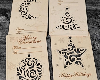 May include: Four wooden greeting cards with decorative cutouts. The cards feature holiday-themed designs, including a crescent moon, Christmas tree, ornament, and star. Each card has space to write "From" and "To" and includes text like "Best wishes" and "Happy Holidays."