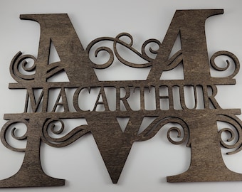 May include: A wooden sign with the last name "MacArthur" cut out in the center of the letters "M" and "M". The letters are decorated with intricate scrollwork.