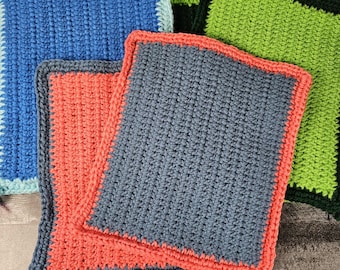 May include: A collection of handmade crochet squares in various colors. The squares are in shades of blue, coral, and green, with contrasting borders. The crochet stitch creates a textured surface. These squares could be used as washcloths or decorative items.