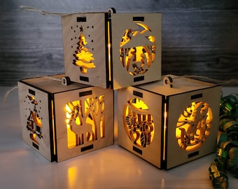 May include: Four wooden Christmas ornaments with different designs. Each ornament has a light inside, creating a warm glow. The ornaments are made of light brown wood and feature a variety of designs, including a Christmas tree, a nativity scene, a reindeer, and a snowflake.