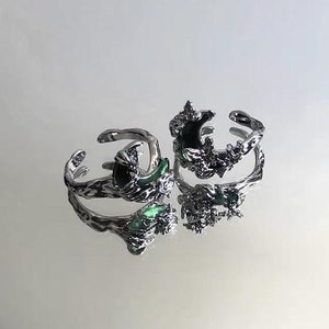 Könnte beinhalten: Zwei silberne Ringe mit einem Halbmond-Design und grüner Emaille. Die Ringe sind mit filigranen Blumenmustern verziert.