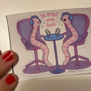May include: A sticker featuring two pink and white striped worms with headphones sitting in chairs and talking into microphones. The text "The Offbeat Worm Podcast" is above the worms. The sticker is on a white background.